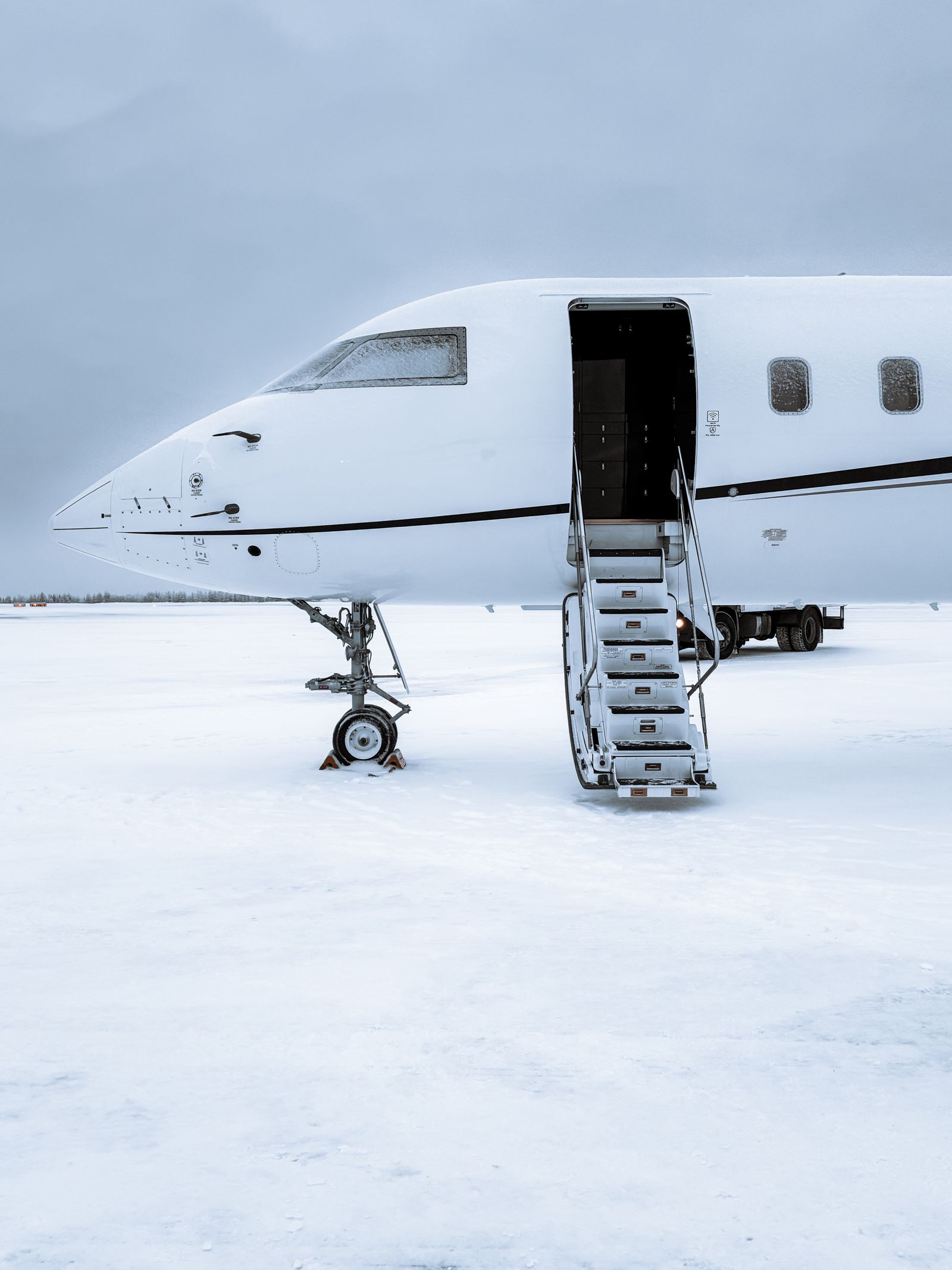 Private jet parked on a snowy runway at dusk with boarding stairs extended