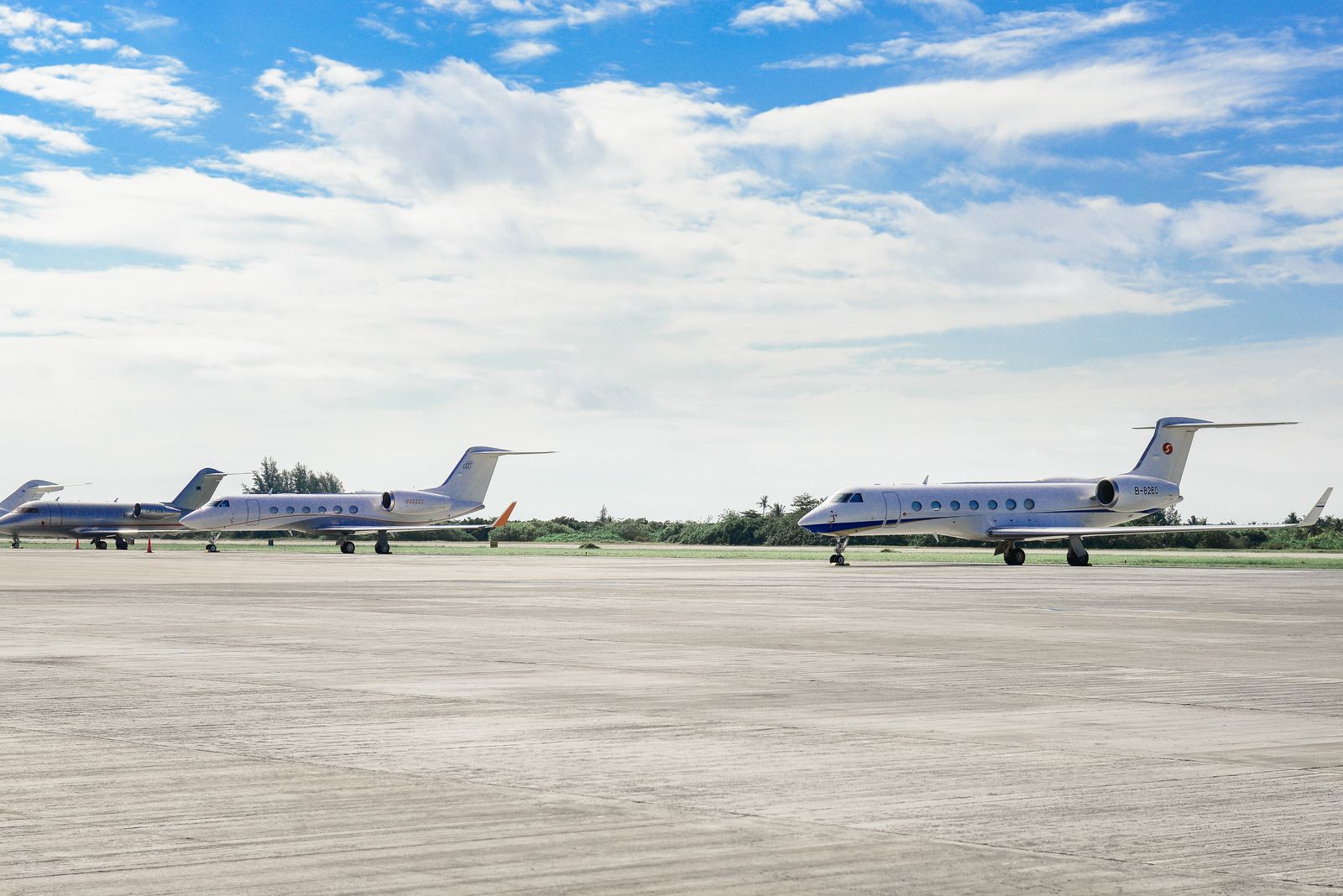 Two business jets parked side by side on a bright airport tarmac under a cloudy sky.